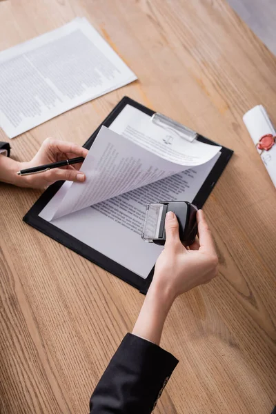 Vue du dessus du notaire recadré avec stylo et tampon près du contrat sur presse-papiers — Photo de stock