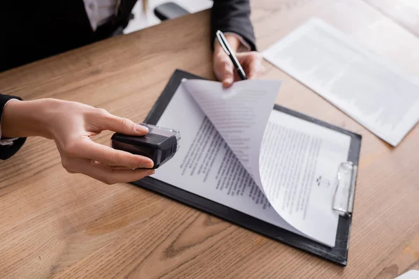 Cropped view of lawyer holding stamper and pen near contract on clipboard — Stock Photo