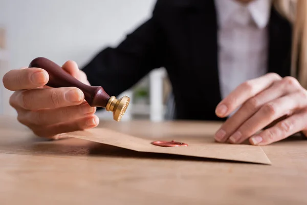 Selective focus of stamper and sealed craft paper envelope in hands of cropped notary on blurred background - foto de stock