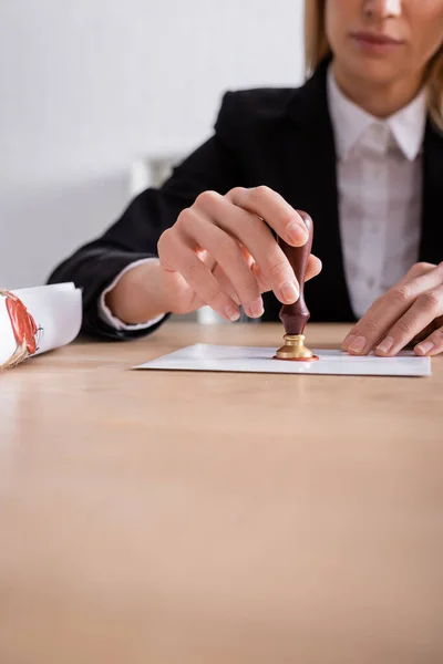 Partial view of notary sealing envelope with wax near rolled contract — Stock Photo