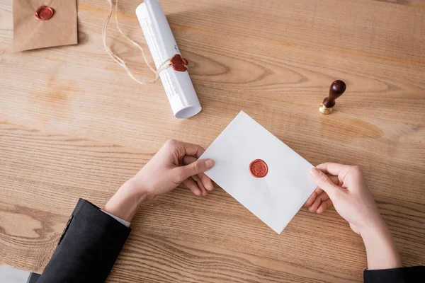 Top view of cropped notary holding sealed envelope near stamper and rolled contract — Stockfoto