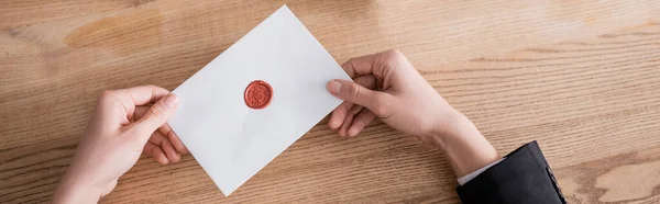 Partial view of lawyer holding enveloped stamped with wax seal near wooden desk, banner — Foto stock