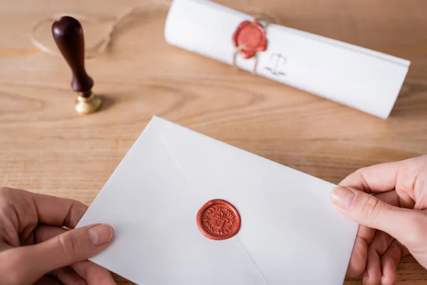 Cropped view of lawyer holding envelope with wax seal near blurred stamper — Foto stock