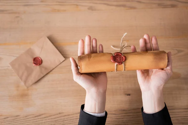 Notaire cultivé tenant parchemin roulé avec joint de cire près enveloppe floue, vue de dessus — Photo de stock