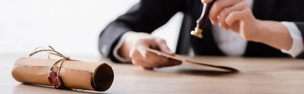 Cropped view of blurred notary stamping envelope near rolled parchment with wax seal, banner — Stockfoto