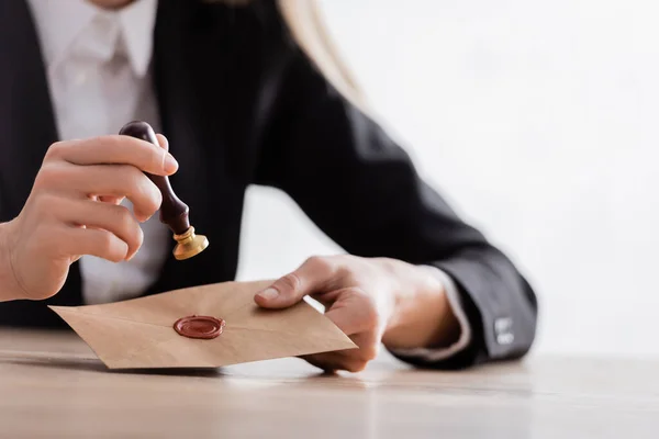 Cropped view of lawyer with stamper and envelope with wax seal on blurred background — Fotografia de Stock