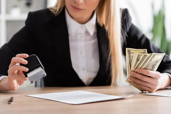 Partial view of notary holding stamper and dollar banknotes on blurred background — стоковое фото