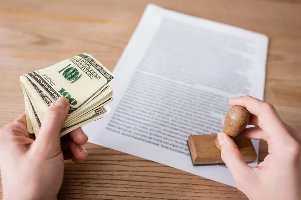 Partial view of notary with dollars and stamper near blurred contract on wooden desk — Photo de stock