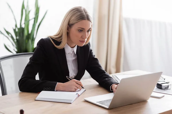 Anwalt arbeitet mit Laptop und hält Stift in der Nähe leeres Notizbuch — Stockfoto