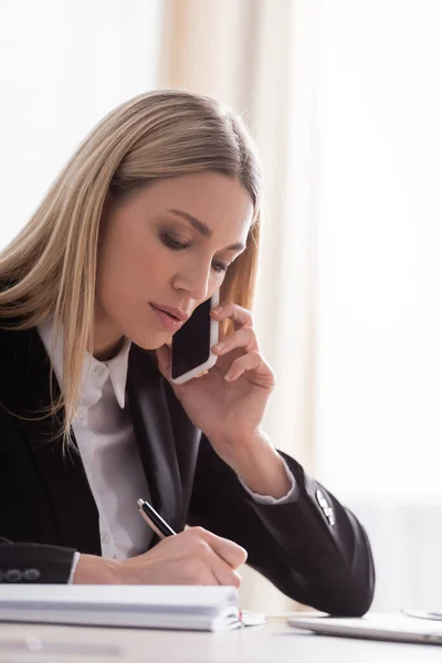 Blonde notary talking on mobile phone and writing in office — Fotografia de Stock