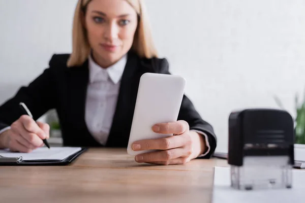 Notario celebración de teléfono inteligente cerca de la estampilla en primer plano borrosa - foto de stock