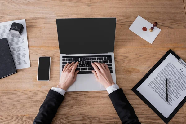 Top view of cropped lawyer typing on laptop near smartphone with blank screen and contract — Stock Photo
