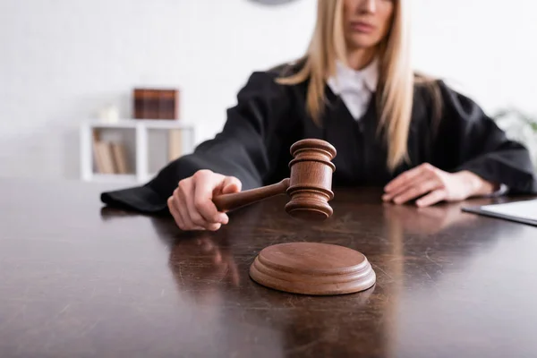 Cropped view of judge holding wooden gavel on blurred background - foto de stock