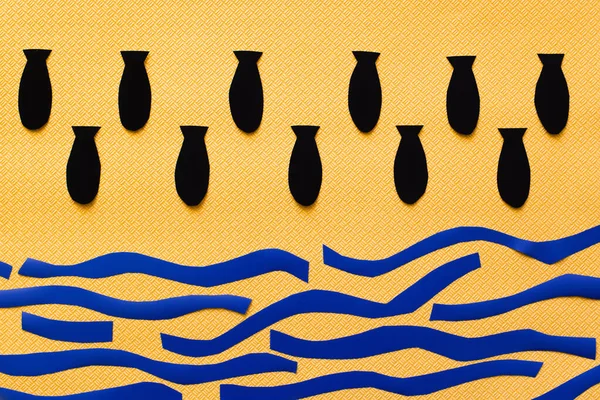 Вид сверху бумажных бомб над картонным морем на текстурированном желтом фоне, война в концептуальном виде — стоковое фото