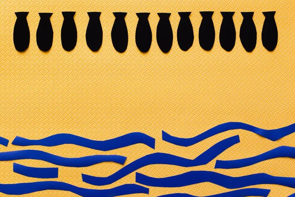 Верхній вигляд ряди з паперовими бомбами над картонним морем на текстурованому жовтому тлі, війна в українській концепції — стокове фото