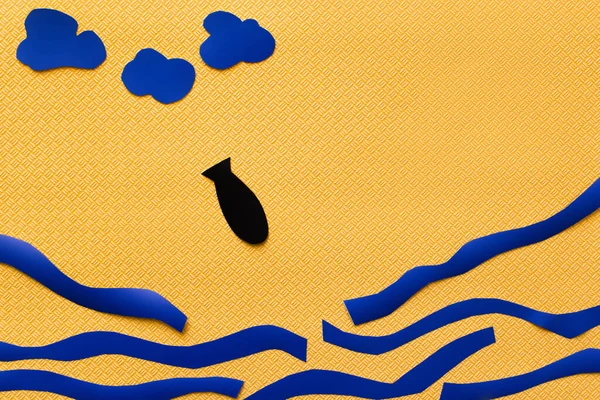 Вид зверху на паперову бомбу біля хмар і картонне море на текстурованому жовтому тлі — стокове фото