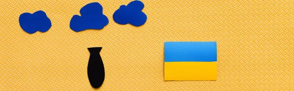 Vista dall'alto di nuvole di carta, bomba e bandiera ucraina su sfondo giallo strutturato, banner — Foto stock