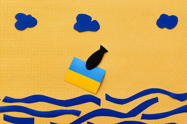 Верхний вид бумажной бомбы возле украинского флага над картонным морем на желтом фоне — стоковое фото