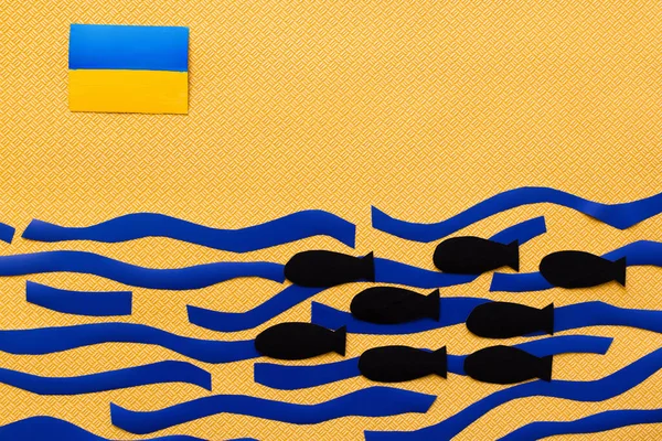 Vista superior da bandeira ucraniana acima da caixa mar e bombas de papel sobre fundo amarelo texturizado — Fotografia de Stock