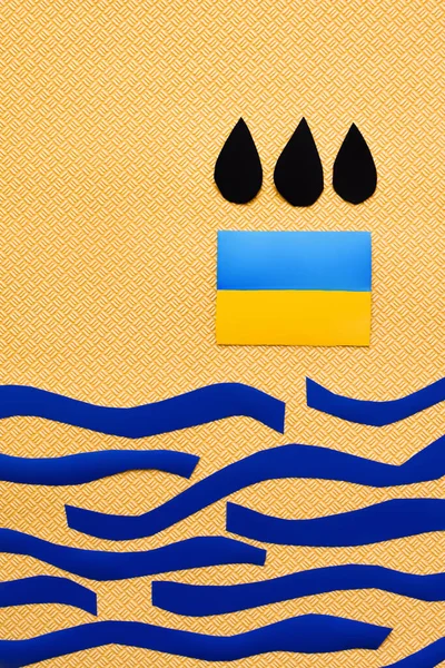 Draufsicht auf schwarze Tropfen über der ukrainischen Flagge und Papiermeer auf strukturiertem gelben Hintergrund — Stockfoto