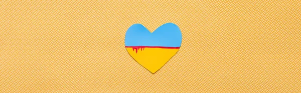 Top view of ukrainian flag with blood in heart shape on textured yellow background, banner — Stock Photo