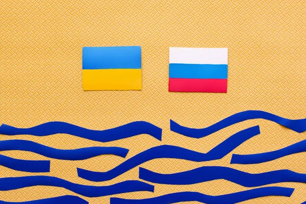 Top view of Ukrainian and russian flags above paper sea on textured yellow background — Stock Photo