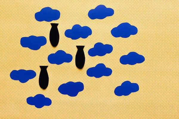Top view of carton clouds and paper bombs on textured yellow background — Stock Photo