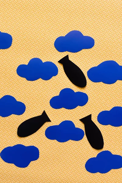 Vue du dessus des bombes en papier près des nuages de carton sur fond jaune texturé, concept de guerre en ukraine — Photo de stock