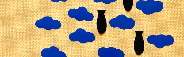 Вид зверху на паперові бомби і картонні хмари на текстурованому жовтому тлі, банер — стокове фото