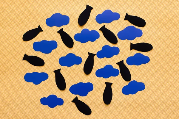 Вид зверху на блакитні картонні хмари та паперові бомби на текстурованому жовтому тлі — стокове фото