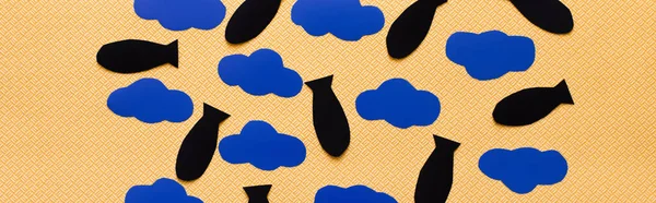 Вид зверху чорних паперових бомб і картонних хмар на текстурованому жовтому тлі, банер — стокове фото