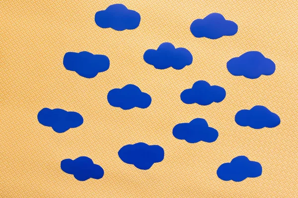 Вид зверху на блакитні паперові хмари на текстурованому жовтому фоні — стокове фото