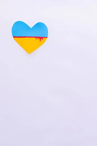 Vista superior de la bandera ucraniana con sangre en forma de corazón sobre fondo blanco con espacio para copiar - foto de stock