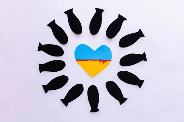 Vue du dessus du drapeau ukrainien en forme de coeur dans le cadre à partir de bombes en papier sur fond blanc — Photo de stock