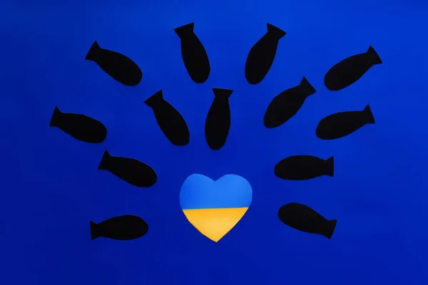 Draufsicht auf Papierbomben über der ukrainischen Flagge in Herzform auf blauem Hintergrund — Stockfoto