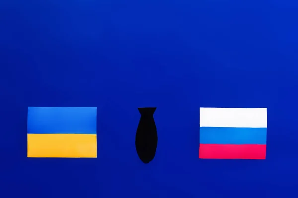 Vue du dessus de la bombe à papier entre les drapeaux ukrainien et russe sur fond bleu — Photo de stock