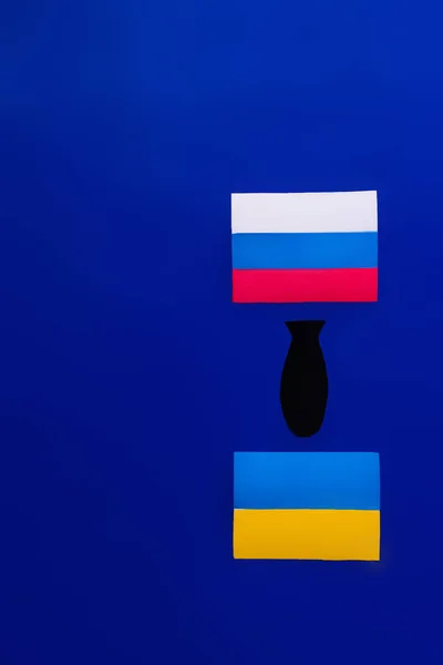 Papierbombe von oben zwischen russischer und ukrainischer Flagge auf blauem Hintergrund — Stockfoto