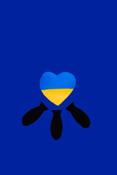 Vue du dessus des bombes en papier sous drapeau ukrainien en forme de coeur sur fond bleu — Photo de stock