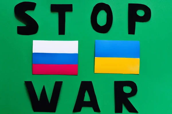 Top view of stop war lettering and ukrainian and russian flags on green background — Stock Photo