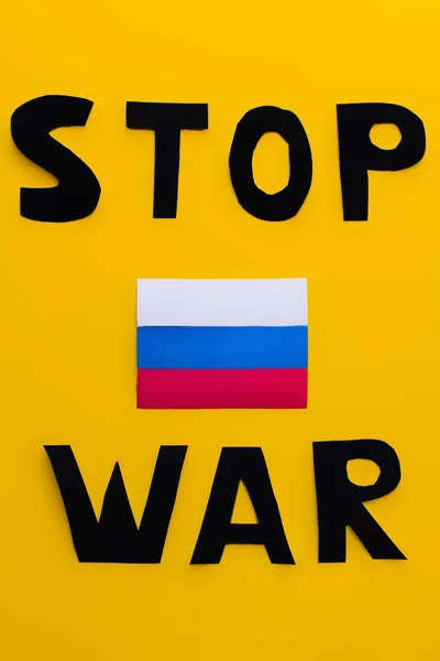 Vista superior de la bandera rusa y dejar de escribir letras de guerra sobre fondo amarillo - foto de stock
