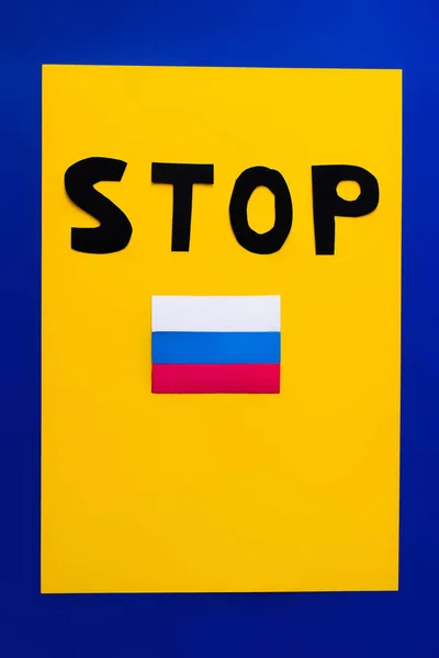 Top view of stop lettering and russian flag on blue and yellow background — Stock Photo