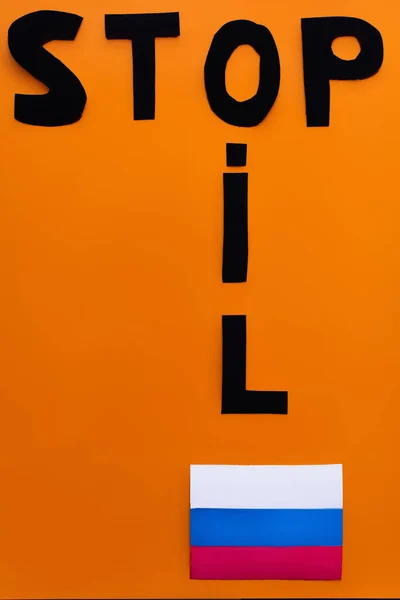 Vista dall'alto di stop e lettering olio vicino bandiera russa su sfondo arancione — Foto stock