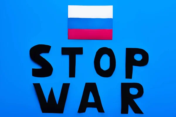 Vista superior de la bandera rusa y dejar de escribir letras de guerra sobre fondo azul - foto de stock