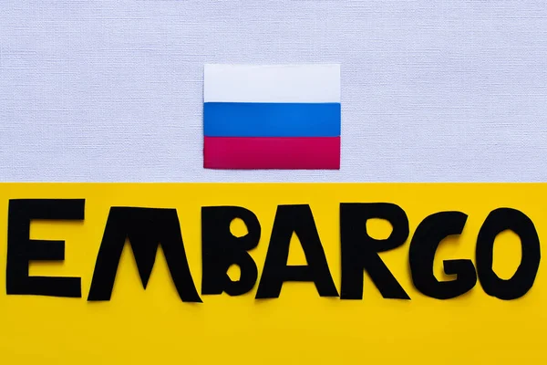 Vista superior da bandeira russa e letras de embargo em fundo branco e amarelo — Fotografia de Stock