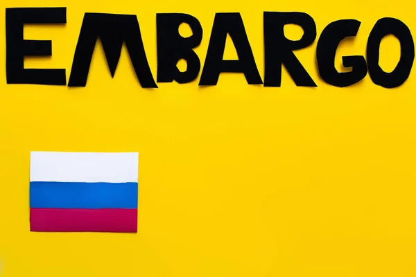 Top view of embargo lettering near russian flag on yellow background, war in ukraine concept — Stock Photo