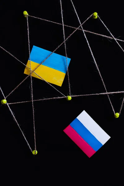 Top view of ukrainian and russian flags near push pins with thread isolated on black — Stock Photo