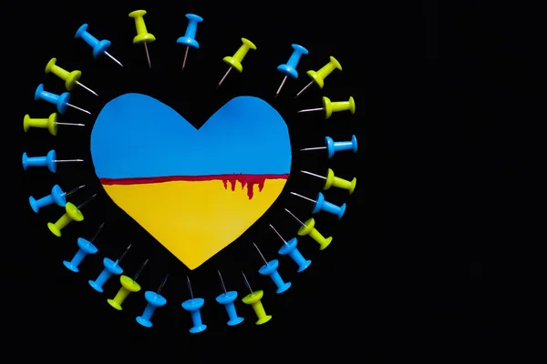 Верхний вид украинского флага с кровью в форме сердца возле булавок, изолированных на черном — стоковое фото