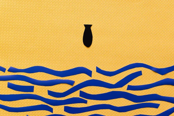 Верхній вид паперової бомби над картонним морем на текстурованому жовтому тлі, війна в українській концепції — стокове фото