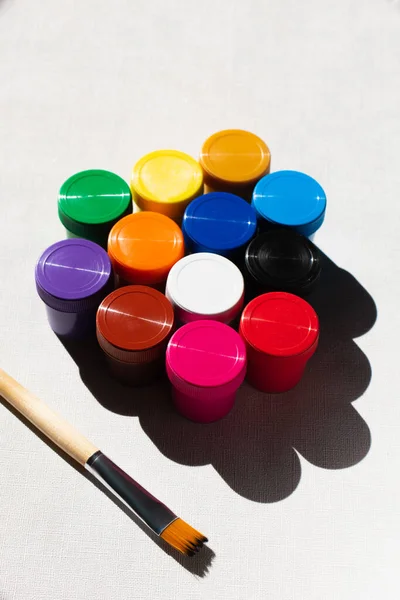 High angle view of paintbrush near jars with colorful paint on white — Stock Photo