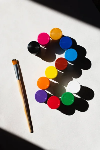 Top view of paintbrush near jars with colorful paint on white — Stock Photo